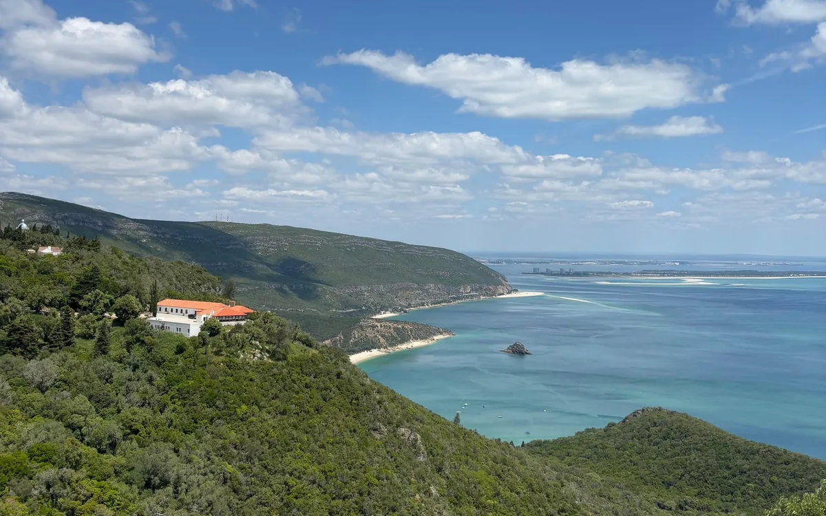 Green wooded hills dropping to a turquoise bay with a strip of pale sand