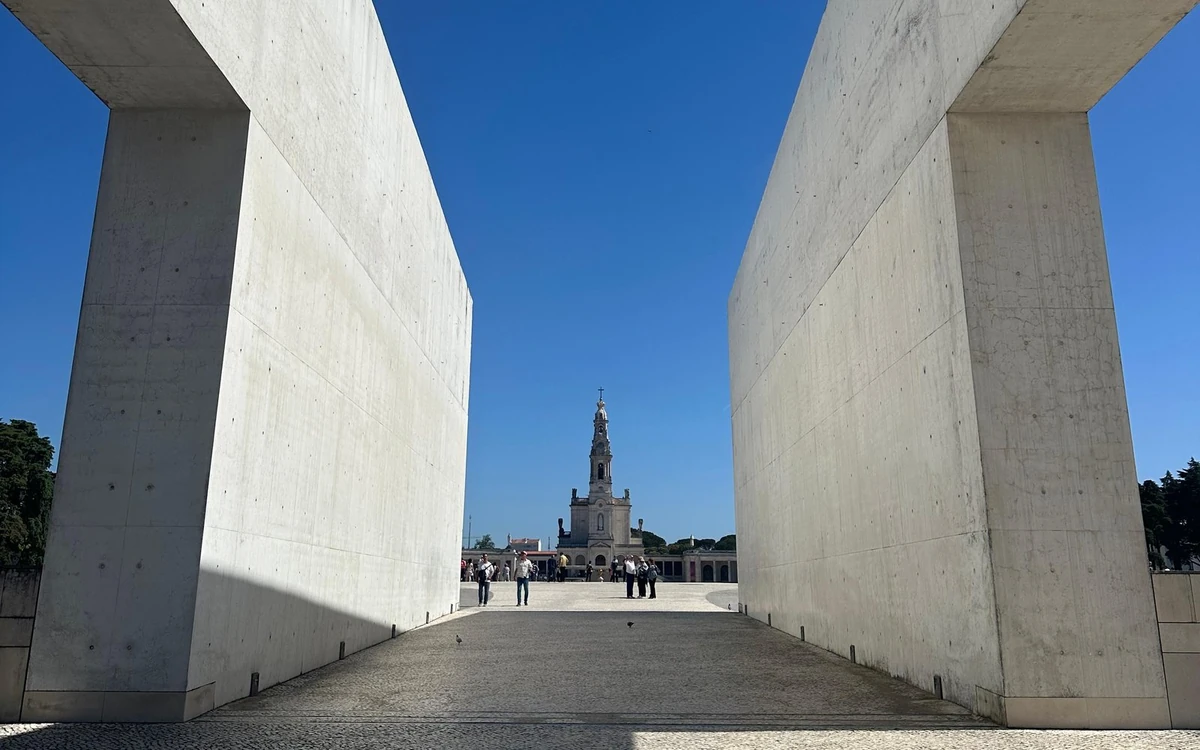 Due alte pareti di cemento incorniciano la torre di una basilica in lontananza attraverso una vasta piazza