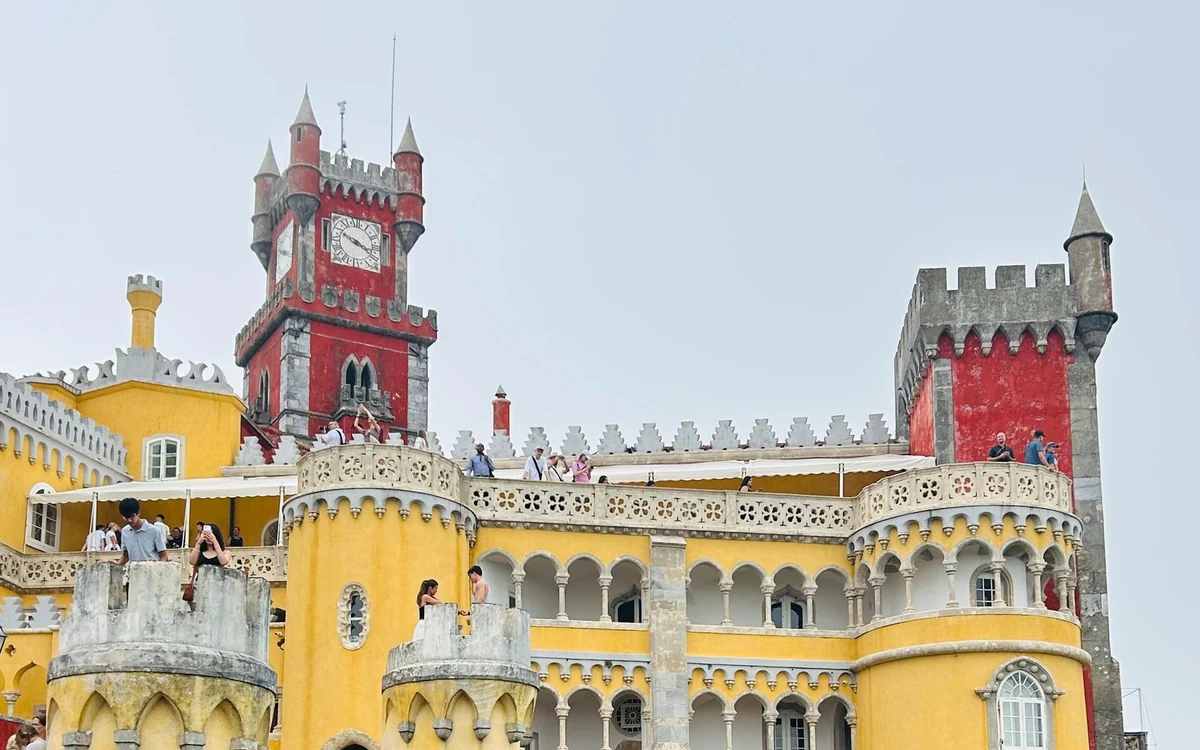 Die gelben Mauern und der rote Uhrturm von Pena Palace, mit Besuchern auf den Terrassen