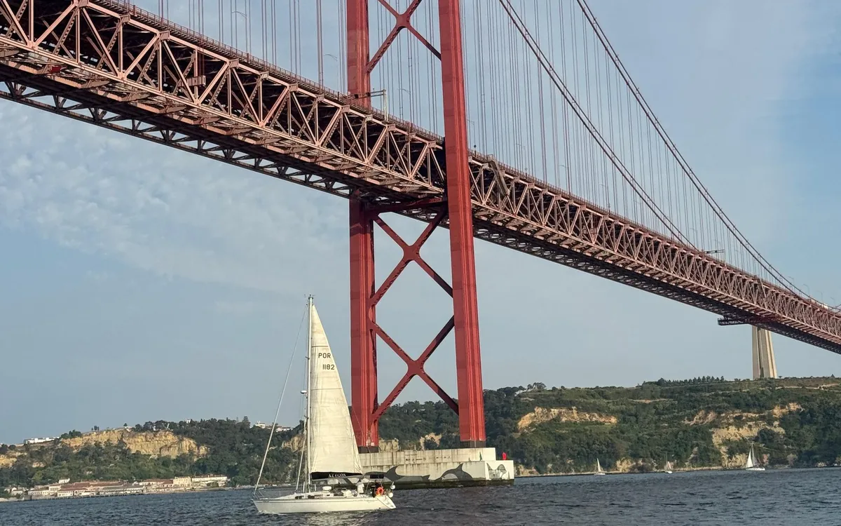 Un velero blanco bajo las torres rojas del Puente 25 de Abril