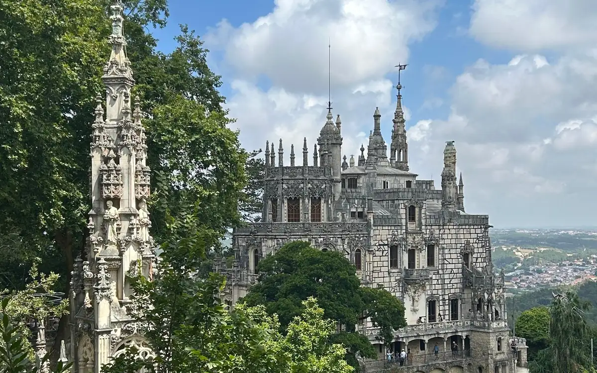 Palais gothique gris aux hautes flèches émergeant des arbres, une ville dans la vallée en arrière-plan