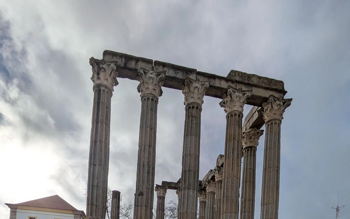 Fluted Roman columns with carved capitals under a cloudy sky in Évora