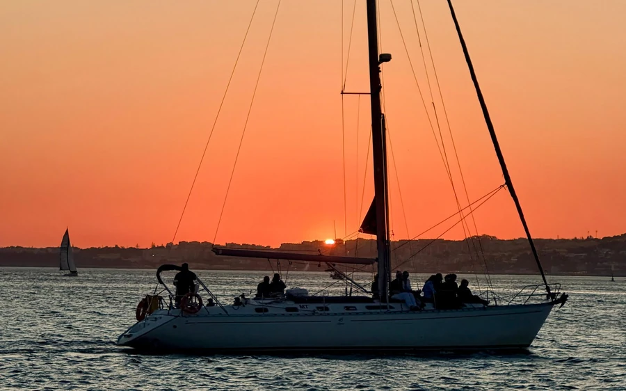 Ein Segelboot mit Personen an Deck, dunkel vor orangefarbenem Himmel