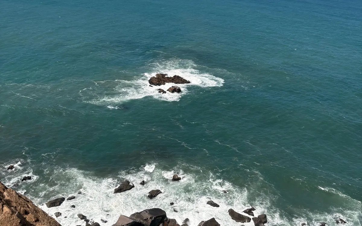 Vista directamente hacia abajo desde un acantilado alto con espuma blanca rompiendo sobre rocas oscuras