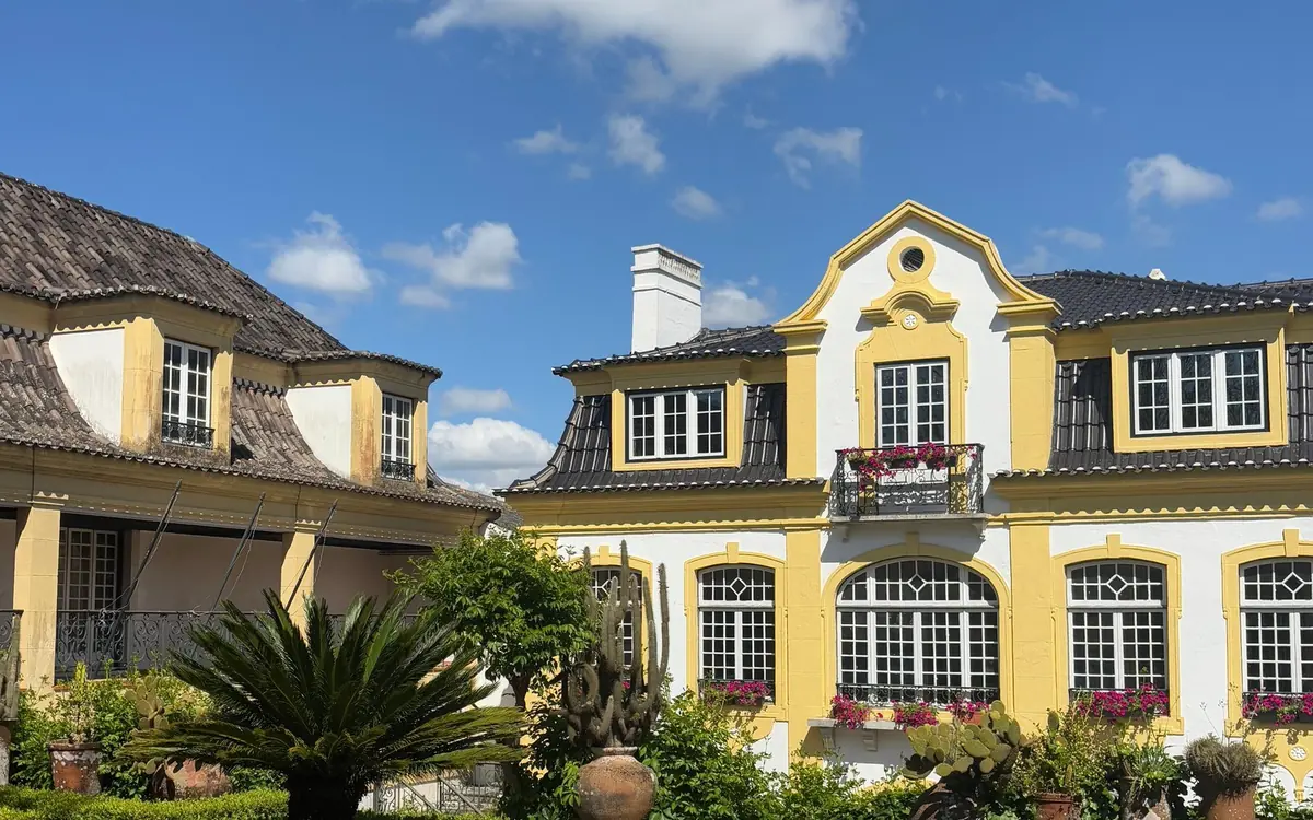 A white manor house with yellow trim and a garden of palms and cacti